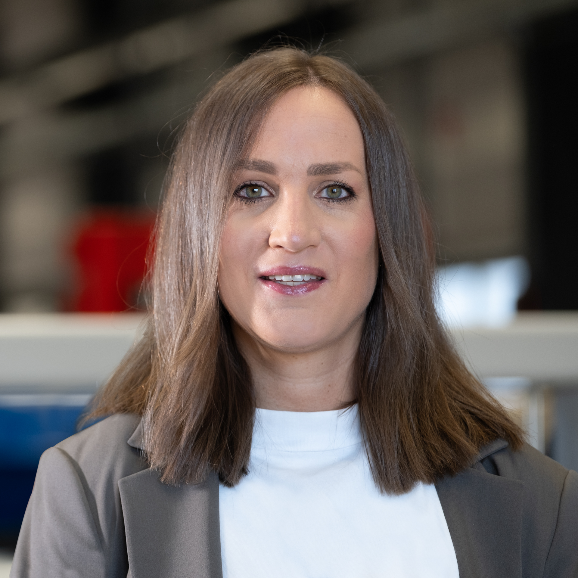 Mitarbeiterin mit braunen Haaren im Blazer in moderner Industrieumgebung.