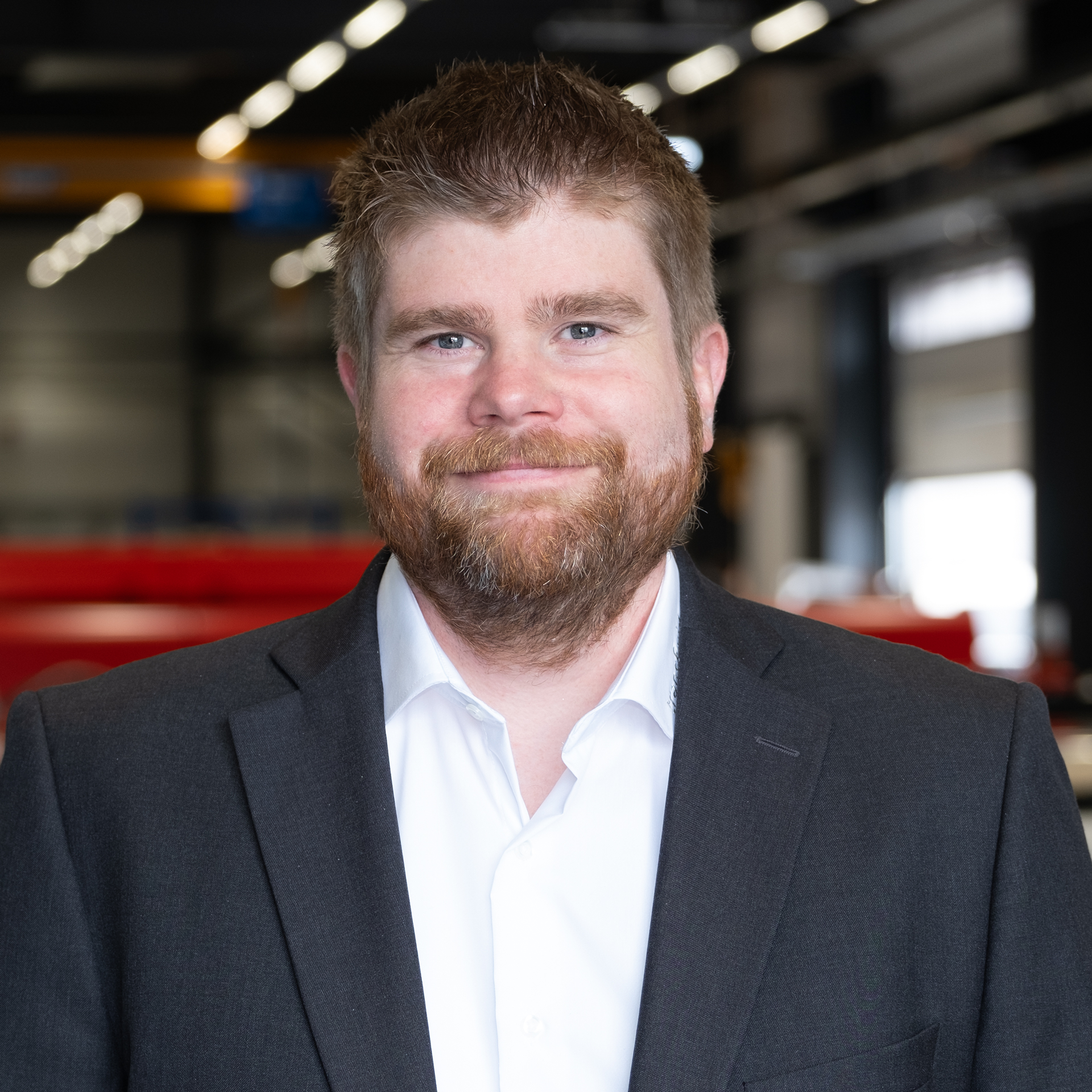 Mitarbeiter im Anzug in moderner Industriehalle mit Maschinen im Hintergrund.