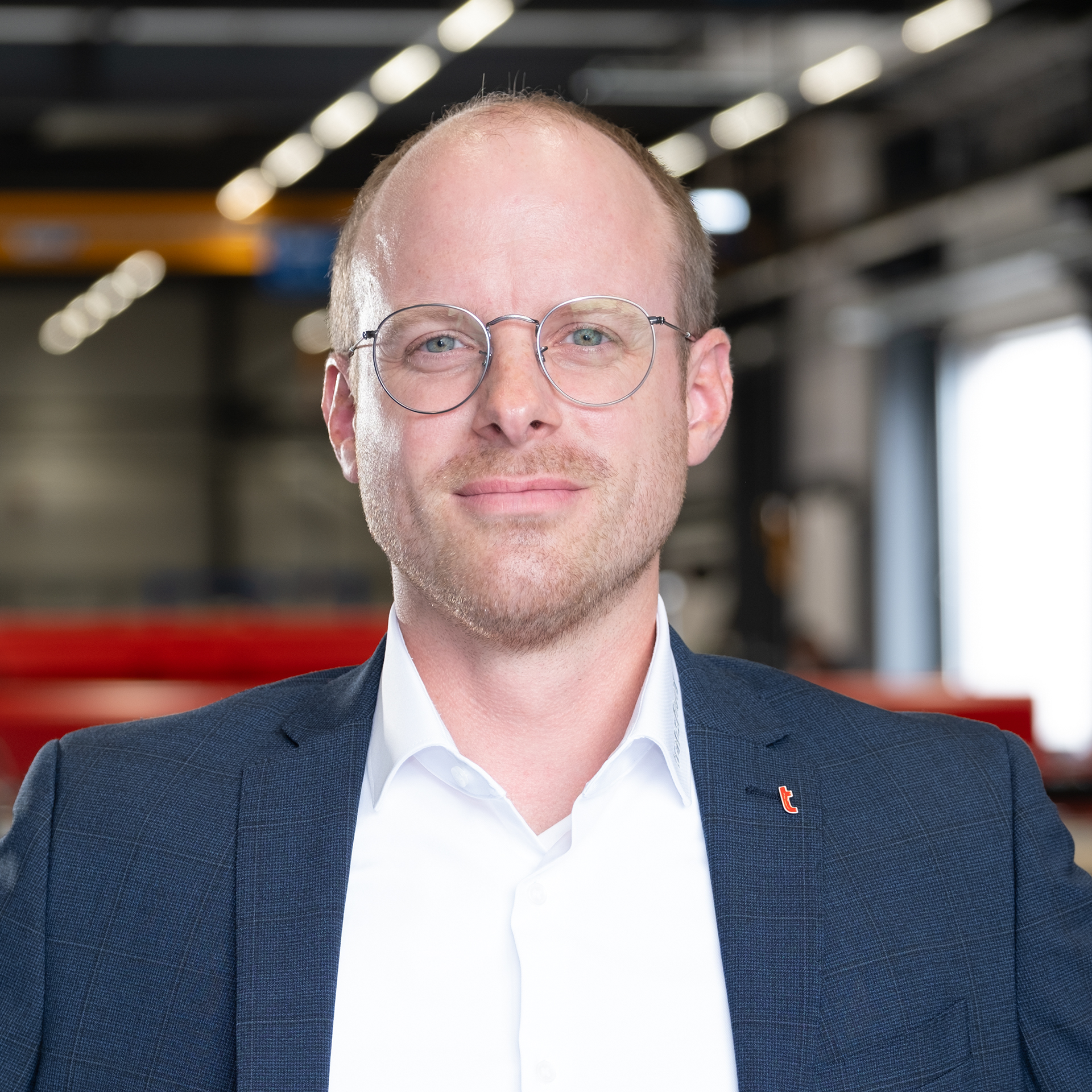 Mitarbeiter mit Brille im Sakko in moderner Industriehalle.
