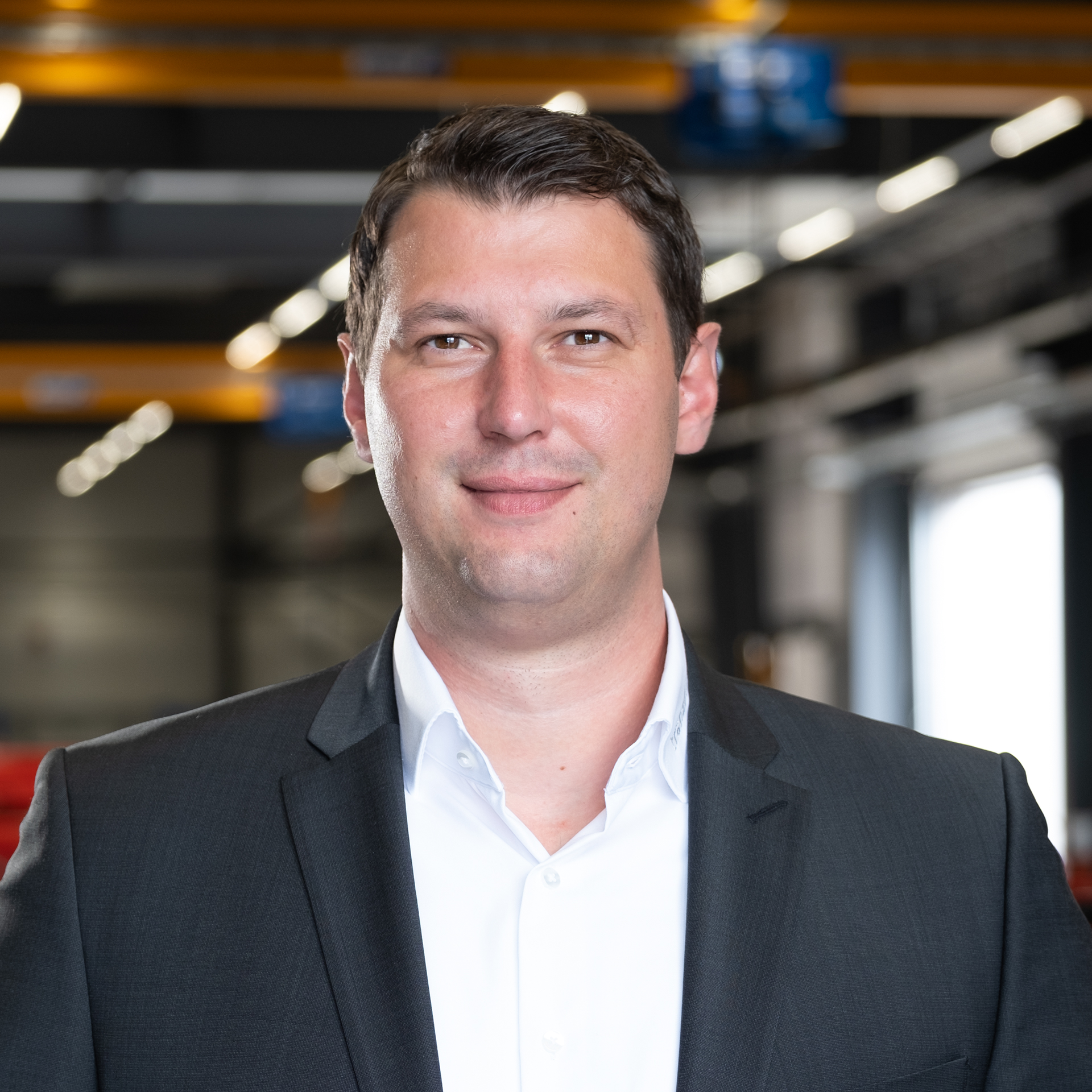 Mitarbeiter im Anzug in moderner Industriehalle mit unscharfem Maschinenhintergrund.